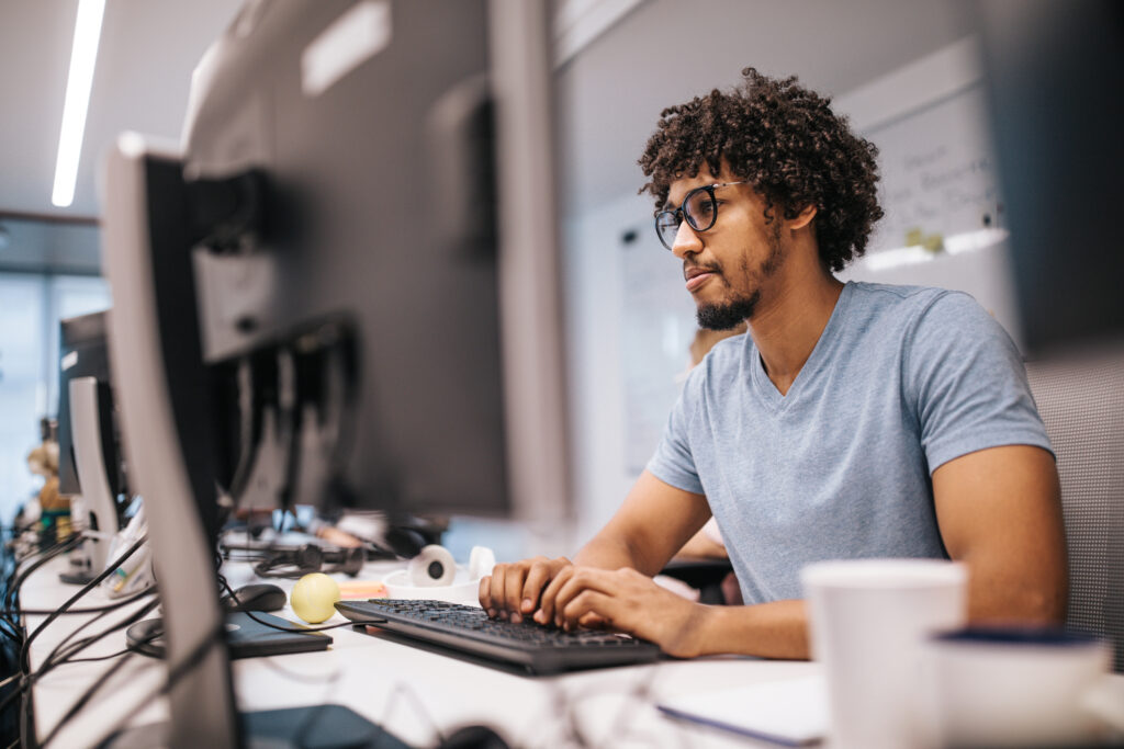 Young black computer programmer coding software while working on PC in the office.