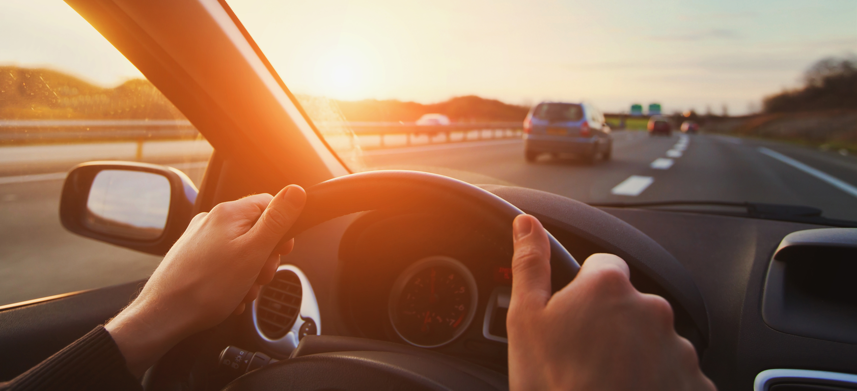 view of the road from the steering when of a car. Hands on the wheel.