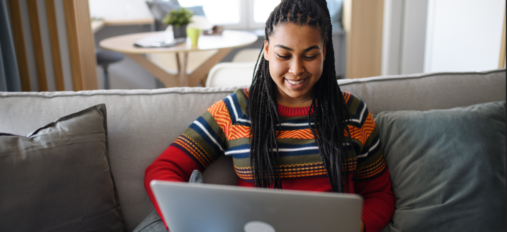 Young woman on her couch smiling with her laptop