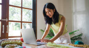 Young woman in yellow on laptop in open living space.