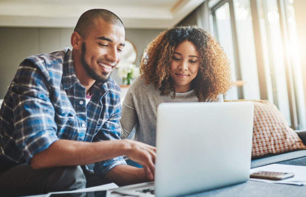 African American man and women sitting on a couch smiling looking at their laptop