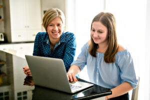 A mother using a laptop in kitchen with teenaget